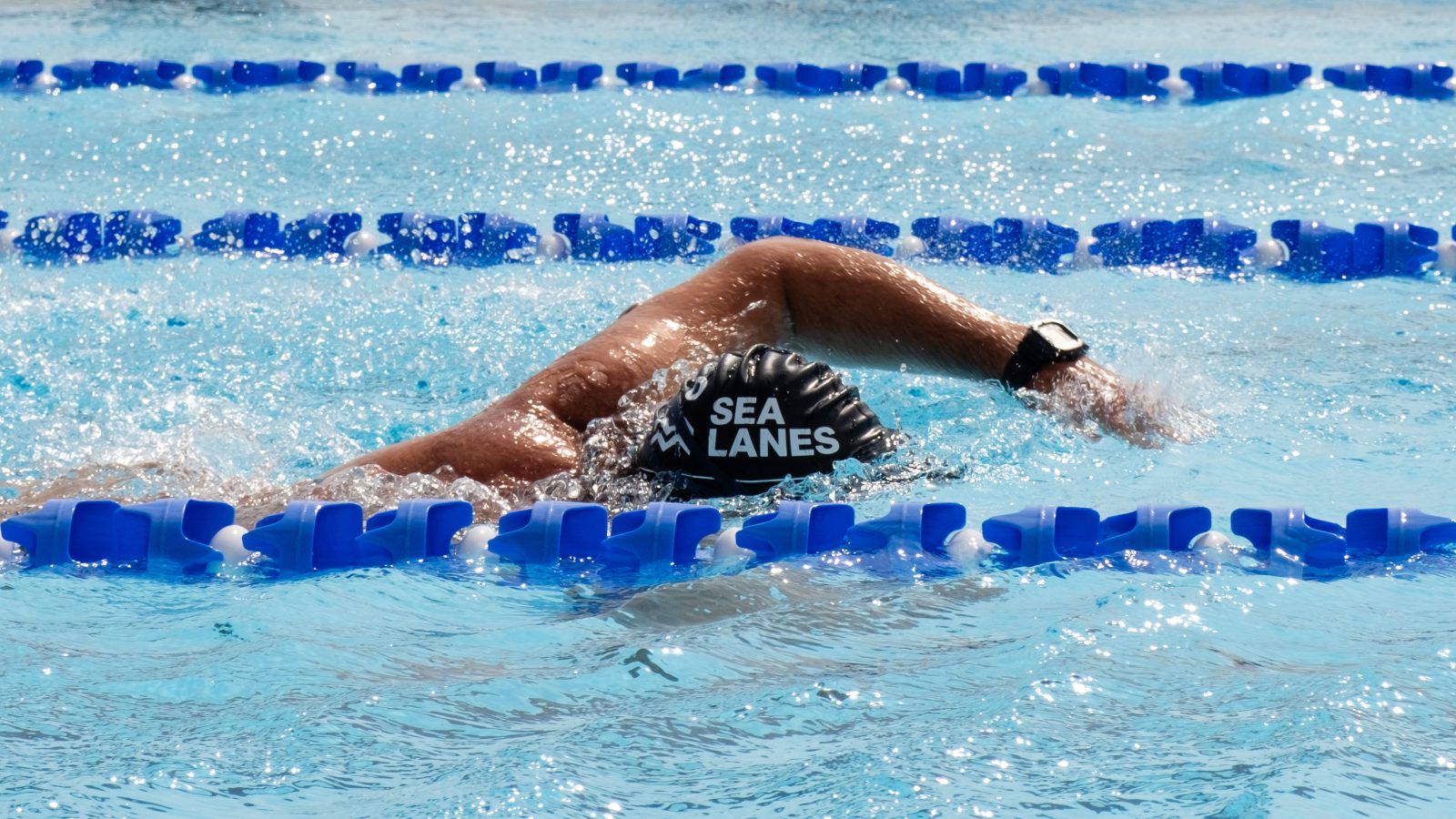 A swimmer doing front-crawl in the pool with a swimming hat saying Sea Lanes on it