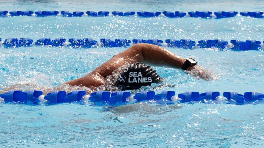 A swimmer doing front-crawl in the pool with a swimming hat saying Sea Lanes on it